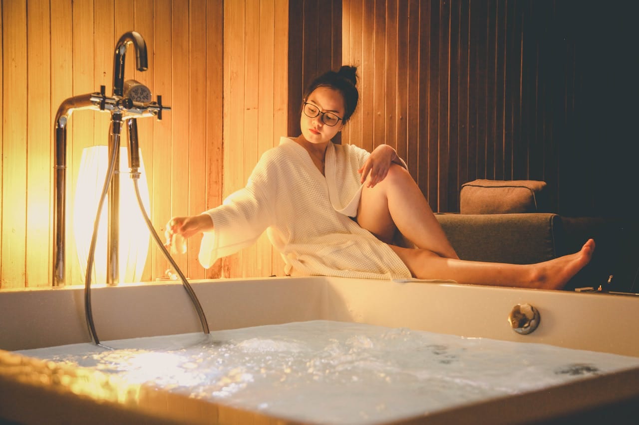 Woman sitting by a jacuzzi in a hotel room, enjoying relaxation indoors.
