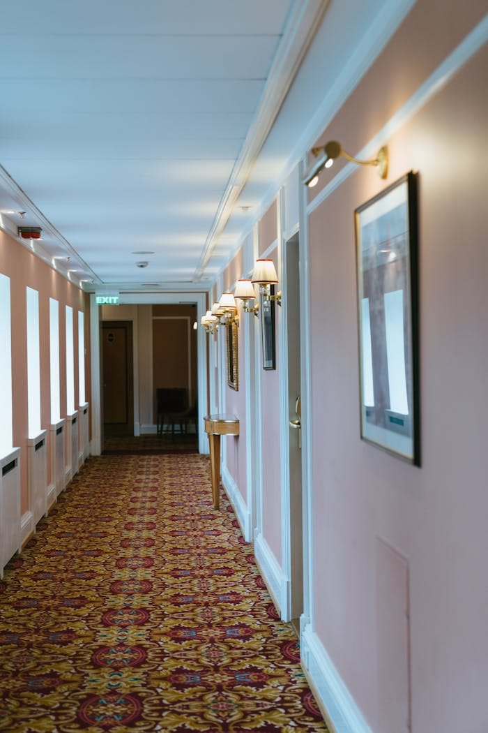 Well-lit hotel corridor with ornate carpet and framed art, offering a cozy atmosphere.